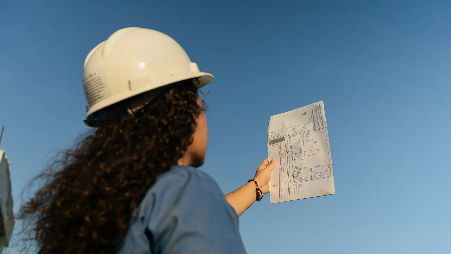 A site lead in a hard hat holds a drawing up against a clear sky.